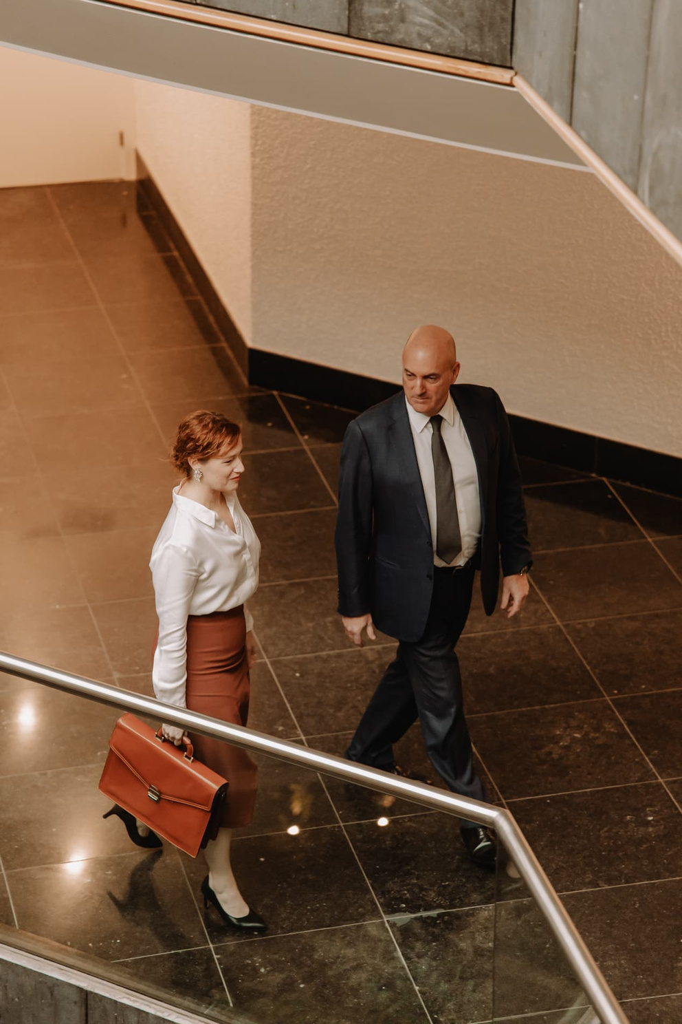 Twee zakelijke mensen lopen samen de trap af in een moderne, lichte kantooromgeving.