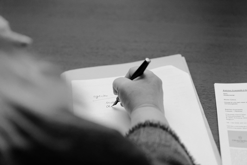 Een hand schrijft met een pen op een vel papier, met een close-up van notities en een document op de achtergrond.