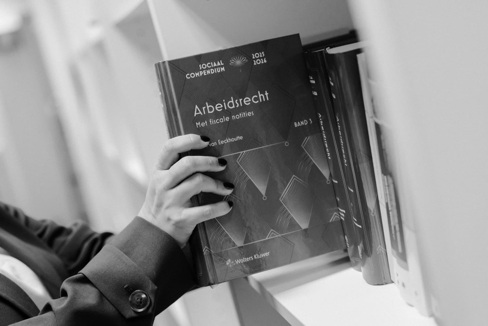 Iemand pakt een boek over arbeidsrecht uit een boekenplank in zwart-wit.